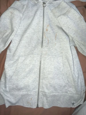 Ljusgrå hoodie med dragkedja - Ljusgrå hoodie med dragkedja framtill och två stora fickor. Tröjan har huva och ribbade muddar vid ärmslut och nederkant. Tillverkad i mjukt sweatshirtmaterial, perfekt för en avslappnad stil.