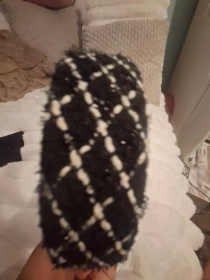 Svart diadem med rutigt mönster - Säljer ett fluffigt svart diadem med vitt rutmönster. Diademet har en bred form och är klätt i ett mjukt, texturerat tyg som ger en trendig look. Insidan är beige och slät för bekväm användning. Perfekt accessoar för att lyfta din outfit.