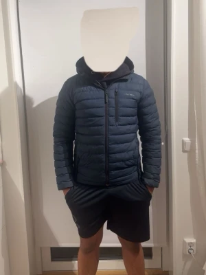 Peak performance jacka  - Snygg mörkblå dunjacka med huva och dragkedja framtill. Jackan har en smal passform, två sidofickor och en bröstficka med dragkedja. Perfekt för kyliga dagar och enkel att matcha med olika outfits.