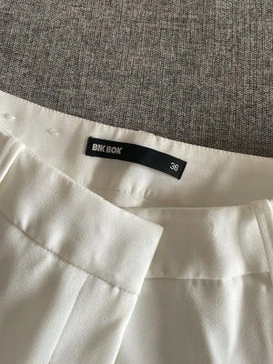 Vita kostymbyxor från Bik Bok - Snygga vita kostymbyxor från Bik Bok i storlek 36. Byxorna har raka ben, pressveck och sidofickor. Endast använd en gång💞