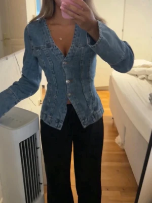 Figursydd blå jeansjacka - Snygg figursydd jeansjacka i klassisk blå denim med V-ringning och silverfärgade knappar framtill. Jackan har långa ärmar och markerad midja för en trendig siluett. Perfekt att styla med både byxor och kjol för en cool look. Passar mig som bruka ha S i vanligt fall