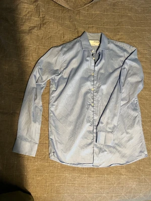 Ljusblå skjorta från Selected Homme - Säljer en stilren ljusblå skjorta från Selected Homme i slim fit. Skjortan har klassisk krage, långa ärmar och knappar framtill. Tillverkad i bomull och perfekt för en clean och fräsch look.