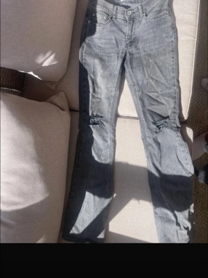 Grå slitna jeans med hål - Säljer ett par grå lågmidkade jeans från perfect jeans i storlek 34. Modellen har raka ben och slitningar med hål på båda knäna för en trendig look. De är i modellen perfect jeans från Gina!