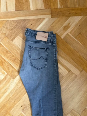 Jacob Cohen jeans  - Säljer ett par gråa Jacob Cohen jeans med klassiska fem fickor. Jeansen har en enkel design med ljus tvätt och smala ben. Perfekta för en avslappnad och trendig look. Materialet är stretchigt för extra komfort.
