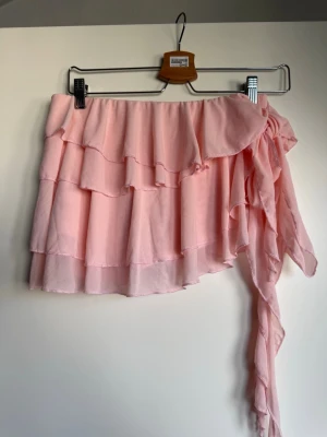 Ljusrosa omlottkjol med volanger - Supersöt ljusrosa kortkjol med omlottdesign och flera lager volanger med inbyggda shorts, har en knytning i sidan  