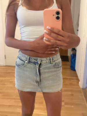 Ljusblå jeanskjol i kort modell - Trendig ljusblå jeanskjol i kort modell med råa kanter och klassiska fickor fram och bak. Kjolen har en avslappnad passform och stängs med dragkedja och knapp framtill. Perfekt till sommaren för en cool och enkel look.