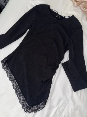 Svart långärmad topp med spetskant - Snygg svart långärmad topp med rund hals och dekorativ spetskant längst ner. Materialet är mjukt och stretchigt, vilket gör den bekväm att bära. Perfekt att styla med jeans eller kjol för en trendig look.