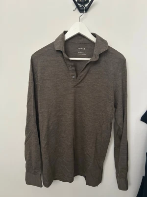 Brun merinoull henley från Boggi - Säljer en brun långärmad henley från Boggi i extra fin merinoull. Skjortan har klassisk krage, knappar vid halsen och en mjuk, tunn känsla. Perfekt för dig som gillar stilrena och bekväma plagg.