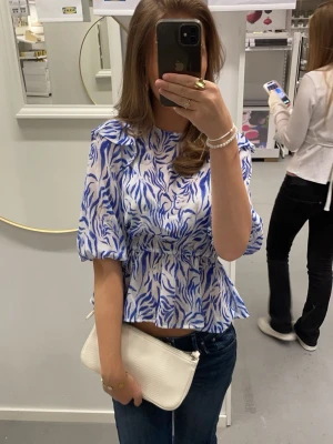Blåvit blus med zebramönster - Säljer en blåvit blus med zebramönster och puffiga korta ärmar. Blusen har en lätt peplumformad midja och rund halsringning. Perfekt för dig som vill sticka ut med ett coolt mönster och trendig siluett.