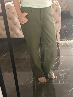 Olivgröna raka jeans - Säljer ett par olivgröna jeans med rak passform och klassisk femficksdesign. Jeansen har normal midja och stängs med knapp och dragkedja. Perfekta för dig som gillar en avslappnad och trendig stil.