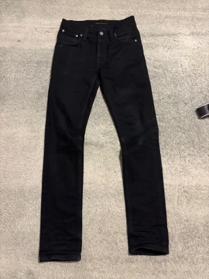 Svarta slim fit jeans - Snygga svarta slim fit jeans med klassisk femficksdesign och raka ben. Jeansen har silverfärgade nitar och knapp, samt diskreta sömmar. Perfekta för dig som gillar en stilren och enkel look. Storlek 28 / 32