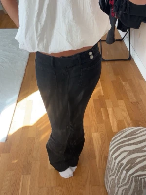 Lågmidjade bootcut jeans - Säljer ett par svarta bootcut jeans med två synliga knappar i midjan och framfickor. Jeansen har en lätt utsvängd passform nedtill och markerade sömmar. Perfekta för dig som gillar en klassisk men trendig look. Längden syns på bild 3 på mig som är 167😊