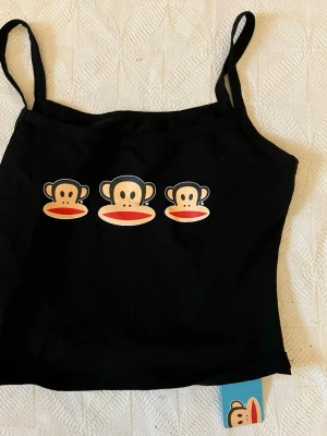 Svart linnetopp Paul Frank x Romwe - Svart linnetopp med smala axelband från Paul Frank x Romwe. Toppen har tre klassiska Paul Frank-apans ansikten tryckta framtill. Perfekt för dig som gillar streetstyle och vill ha något lekfullt i garderoben.
