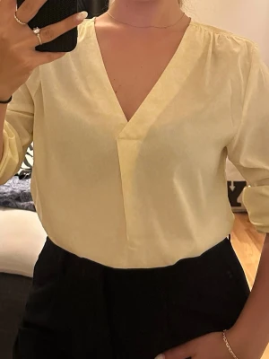 Ljusgul blus med v-ringning - Snygg ljusgul blus med djup v-ringning och långa ärmar. Blusen har en lös passform och lätt glansigt material som ger en fräsch look. Perfekt att styla med både jeans och kjol för en trendig outfit.