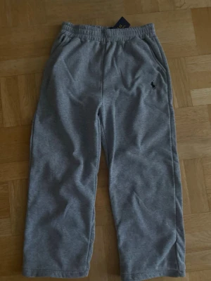 Grå mjukisbyxor från Polo Ralph Lauren - Snygga grå mjukisbyxor från Polo Ralph Lauren med klassisk logga broderad på vänster sida. Byxorna har resår i midjan och sidofickor. Perfekta för chill dagar och gjorda i mjukt material som känns skönt mot huden.