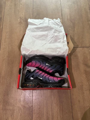 Helt nya Nike Air Max Plus TN (Rosa/Svart) - Strl 39 🔥✨ - Säljer ett par grymma och helt nya Nike Air Max Plus (TN) i en snygg färgövergång från rosa till svart. Skorna är aldrig använda, kommer med originalkartong och tagsen sitter kvar!  Storlek: 39  Skick: Helt nya / Deadstock (DS) i box  Färg: Black/Pink Gradient  Kvitto: Saknas Skickas spårbart eller hämtas enligt överenskommelse. Köparen står för frakten. Skriv ett DM om du har några frågor eller vill ha fler bilder! 👟💨 