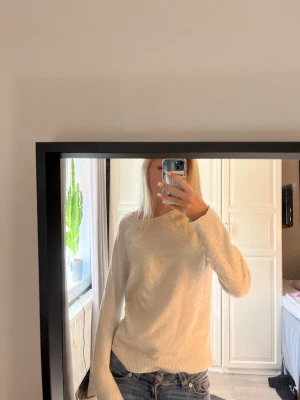 Beige stickad tröja - Mysig beige stickad tröja med rund halsringning och långa ärmar. Tröjan har ribbade muddar vid ärmslut och nederkant, vilket ger en snygg och avslappnad look. Perfekt att matcha med jeans för en enkel och stilren outfit.