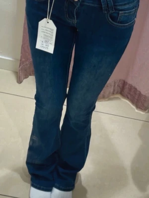 Mörkblå bootcut jeans - Snygga mörkblå bootcut jeans med klassisk femficksdesign och lätt slitna detaljer framtill. Jeansen har låg midja och är tillverkade i ett stretchigt denimtyg som ger en bekväm passform. Perfekta för en trendig och avslappnad look.