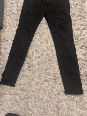 Svarta slim fit byxor - Säljer ett par svarta slim fit byxor med klassisk femficksdesign och diskreta sömmar på bakfickorna. Byxorna har smal passform och är tillverkade i ett stretchigt material som ger en bekväm känsla. Perfekta till en avslappnad stil.
