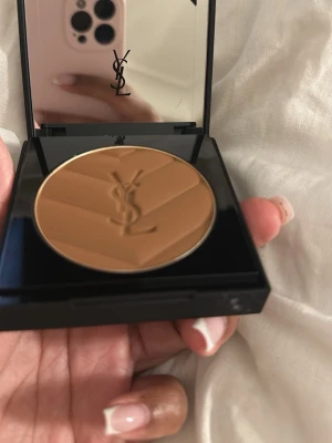 YSL bronzer i lyxig brun dosa - Snygg bronzer från YSL i en elegant brun dosa med guldigt YSL-logo. Pudret har en varm, gyllenbrun ton och är pressat i ett chevronmönster med logotyp i mitten. Perfekt för att ge ansiktet en solkysst look och kommer i en exklusiv förpackning. OBS! Den är endast använd en gång och jag tyckte inte att den matchade min färg tyvärr. Annars riktigt otrolig