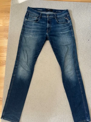 Mörkblå jeans i slim-fit modell - Snygga mörkblå slim fit jeans från replay i modell anbass. Tvättade detaljer, klassisk femficksmodell med dragkedja och knapp i midjan. Jeansen har smal passform och personen på bild är 193cm lång.