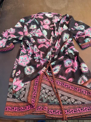 Mönstrad kortklänning från Esprit - Säljer en färgglad kortklänning från Esprit med svart bas och blommigt paisleymönster i rosa, turkos och lila. Klänningen har snörning i midjan, v-ringning och trekvartsärm. Perfekt för dig som gillar boho-vibbar och unika detaljer.