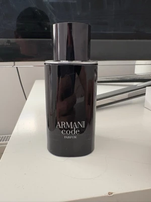Armani Code Parfum - Säljer en stilren parfymflaska från Armani Code Parfum. Flaskan är svart och cylinderformad med en elegant, minimalistisk design och tydlig logga framtill. Perfekt för dig som gillar exklusiva dofter och vill ha en snygg flaska på hyllan.