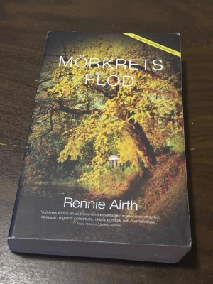 Mörkrets flod av Rennie Airth - En spännande pocketbok med titeln 'Mörkrets flod' av Rennie Airth. Omslaget har ett höstigt motiv med gula löv och en stig som leder mot ett litet vitt tempel. Boken är tryckt på vanligt papper och ges ut av Bokförlaget Minotaur.