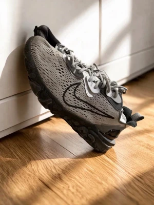 Grå Nike sneakers med svart sula - Snygga grå sneakers från Nike med svart sula och svart swoosh på sidan. Ovandelen är i meshmaterial med prickiga detaljer och skorna har gråa skosnören. Perfekta för dig som gillar sportig och modern stil.