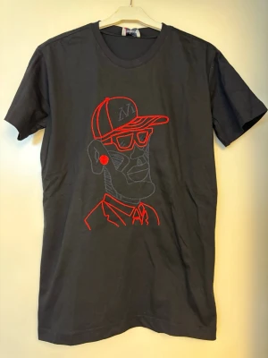T-shirt med broderat tryck på. - Svart t-shirt med broderat tryck på. Se sista bild för att se trycket i närbild. Lapp kvar, så aldrig använd!
