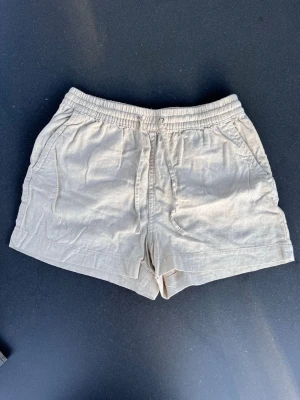 Beiga linneshorts - Snygga beiga linneshorts med avslappnad passform och resår i midjan. Shortsen har snedställda fickor fram och två dekorativa fickor bak. Perfekta för varma dagar och ger en chill vibe till din outfit.