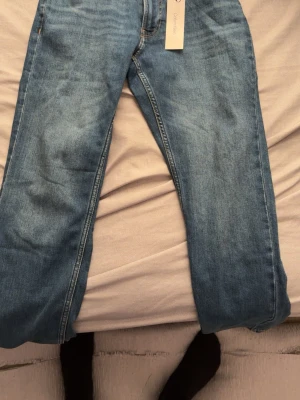 Blå raka jeans i klassisk modell - Säljer ett par blå jeans i klassisk rak modell med normal midja. Jeansen har fem fickor och är tillverkade i ett mjukt denimtyg. Perfekta för dig som gillar en enkel och tidlös stil.