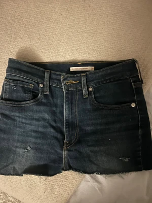 Levi's jeanskjol mörkblå - Säljer en mörkblå jeanskjol från Levi's med slitna detaljer. Klassisk femficksmodell med Levi's patch bak och röd etikett på ena bakfickan. Perfekta för en avslappnad och trendig look. Jag köpte de som ett par jeans men de var för små så jag gjorde om den till en jeanskjol så därför är inte storleken 28 längre eftersom att de var högmidjade innan. Jag skulle gissat på 24-25