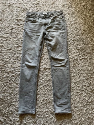 Grå slim fit jeans från 157 - Snygga grå slim fit jeans från 157 med klassisk femficksdesign och smal passform. Jeansen har bälteshällor, dragkedjegylf och är tillverkade i ett mjukt denimtyg som sitter skönt hela dagen. Perfekta för en avslappnad och trendig look.