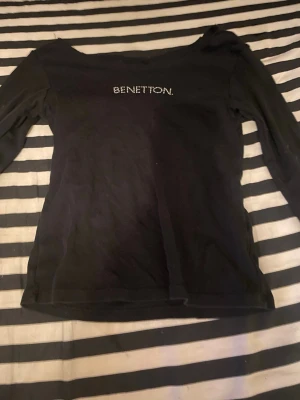Svart långärmad topp från Benetton - Säljer en svart långärmad topp från Benetton med Benetton-loggan i små glittriga stenar på bröstet. Toppen har en klassisk, enkel passform och är perfekt att styla med jeans eller kjol. Materialet känns mjukt och bekvämt mot huden. Med storlek 140