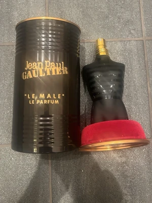 Jean Paul Gaultier Le Male Parfym 75ml - nästan oanvänd 75ml Ikonisk parfymflaska formad som en manlig torso i svart frostat glas med guldfärgad spray och detaljer. Kommer med en svart metallcylinder med guldfärgad text och röd sammetsbotten. Doften är djärv och maskulin.