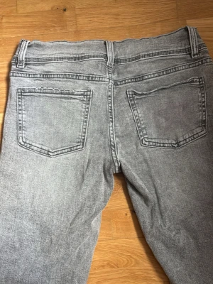 Lowwaist Grå raka jeans med tvättad look - Snygga grå jeans med tvättad effekt och raka ben. Jeansen har klassiska bakfickor och normal midja. Perfekta för en avslappnad och trendig stil. Materialet känns som klassisk denim och färgen är en ljusgrå nyans.