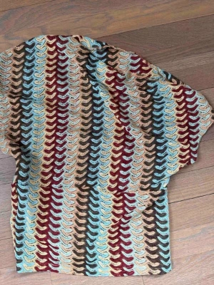 Mönstrad stickad topp i retrostil - Unik stickad topp med färgglatt mönster i blått, vinrött, beige och brunt. Toppen har korta ärmar och ett vågigt, nästan retroinspirerat mönster som verkligen sticker ut. Perfekt för dig som vill ha något annorlunda och färgglatt i garderoben.
