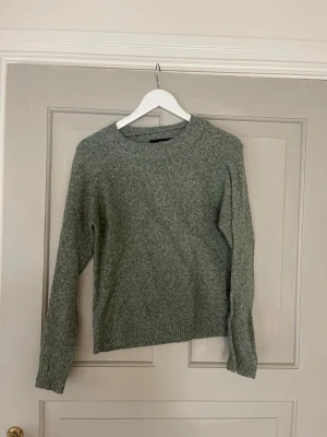 Grågrön stickad tröja Vero Moda - Mysig grågrön stickad tröja från Vero Moda i storlek XS. Tröjan har rund halsringning, långa ärmar och ribbade muddar vid ärmslut och nederkant. Perfekt för kyliga dagar och enkel att matcha med jeans eller kjol.