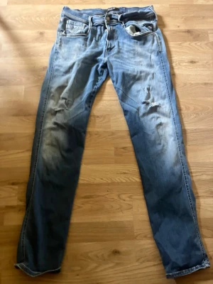 Replay anbass - Säljer ett par blå skinny jeans med slitningar och en trasig detalj på höger lår. Jeansen har klassisk femficksdesign och är tillverkade i denim med tvättade partier för en cool, använd look. Perfekta för dig som gillar en avslappnad och trendig stil.