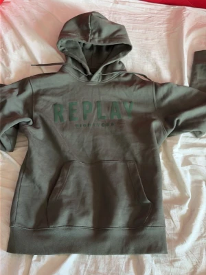 Replay Hoodie - Snygg grön hoodie från Replay med stor ficka framtill och huva. Trycket 'REPLAY EIGHTY ONE' syns på bröstet. Mjuk insida och ribbade muddar vid ärmslut och nederkant. Perfekt för en avslappnad och trendig look. Nästan oanvänd