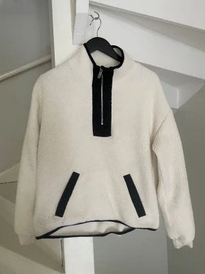 Vit teddyjacka - Mysig vit teddyjacka med halv dragkedja framtill och svarta detaljer vid dragkedja, fickor och nederkant. Jackan har hög krage och två snedställda fickor. Perfekt för kalla dagar och riktigt skön att bära. Passar även storlek S. Pris går att diskuteras 