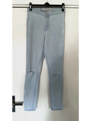 Denim Co - Ljusa skinny jeans med slitningar - storlek 40 - Säljer ett par ljusblå skinny jeans med hög midja och slitningar vid knäna. Jeansen har klassisk femficksdesign och är tillverkade i stretchigt denimtyg för en bekväm passform. Perfekta för en avslappnad och trendig look.