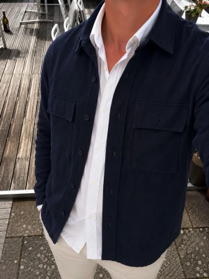 Samsøe Samsøe Marinblå Overshirt / Utility Shirt – Strl S - Snygg marinblå overshirt från Samsøe Samsøe i en stilren utility-modell. Perfekt som ett lager över en skjorta eller T-shirt och passar lika bra till vardags som till en mer dressad outfit.  • Marinblå färg • Utility-inspirerad design • 2 bröstfickor med lock • Klassisk krage • Knäppning framtill • Justerbara ärmslut • Samsøe Samsøe • Storlek S • Modell: KXS63900 / Style: Q9SM412804 • Färg: Sky Captain  Mycket lättmatchad och tidlös modell. Se bilder för skick och alla detaljer.