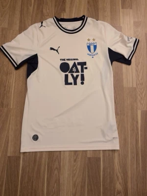 Malmö FF vit matchtröja Puma - Snygg beige matchtröja från Malmö FF med svarta detaljer och tryck från Malmö ff affär. Storlek Xs men passar även S