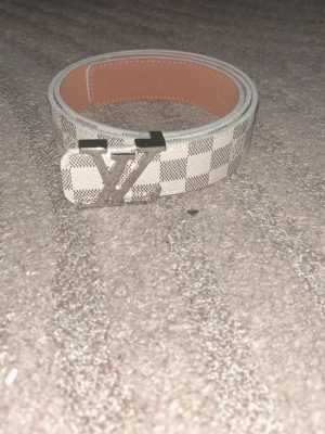 Vit rutig bälte med silverdetaljer - Snyggt vitt bälte med rutigt mönster och Bältet har en klassisk design och är perfekt för att lyfta vilken outfit som helst. Insidan är beige och materialet känns lyxigt. Pris kan diskuteras