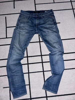 Blå slitna jeans med raka ben - Säljer ett par Replay jeans med snyggt slitna detaljer och raka ben. Jeansen har klassisk femficksdesign, dragkedjegylf och kontrastsömmar. Perfekta för en avslappnad och trendig look. Storlek 30/32
