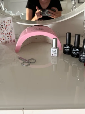 Nagellack-kit med UV-lampa och dekaler - Komplett nagellack-kit med rosa UV-lampa, basecoat och topcoat samt ett nagellim. Nagellacken är röda och en vit samt en ljusrosa från depen, juliga nageldekaler med tomtar och renar samt sax och tippar. Perfekt för att fixa snygga gelnaglar hemma och dekorera med söta motiv.