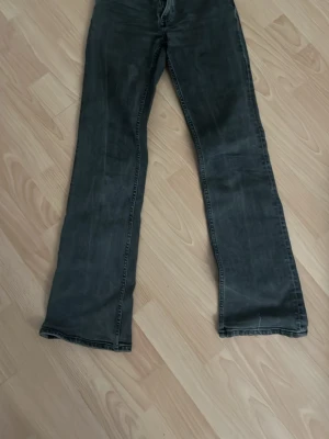 Svarta bootcut jeans med slitningar - Säljer ett par svarta bootcut jeans med lätt slitna detaljer och klassisk femficksmodell. Jeansen har en något utsvängd passform nedtill och är tillverkade i denim med stretch. Perfekta för dig som gillar en retro vibe och vill ha ett par bekväma jeans med cool look.