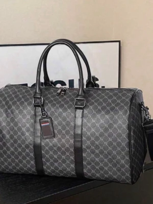 Svart weekendbag med mönster - Snygg svart weekendbag med diskret mönster och svarta detaljer. Väskan har dubbla handtag, avtagbar axelrem och en tag i läder-look. Perfekt för resor eller gymmet, med rymligt huvudfack och dragkedja. Materialet ser ut att vara konstläder eller canvas.